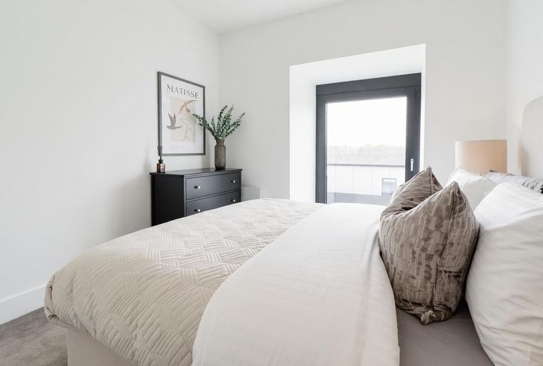 A bedroom with a bed, pillows, a dresser, and a window.