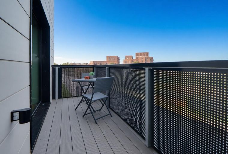 A balcony with a table, chairs, and a view of buildings under a blue sky.