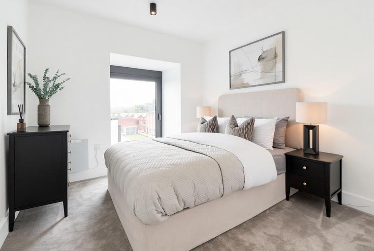 A bedroom with a bed, bedside tables, a dresser, and a window.