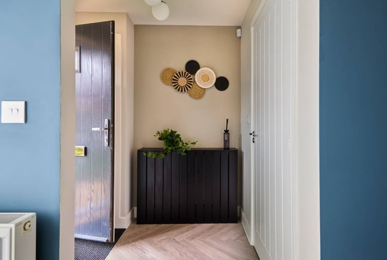 A hallway with a dark radiator cover, woven wall art, and two doors.