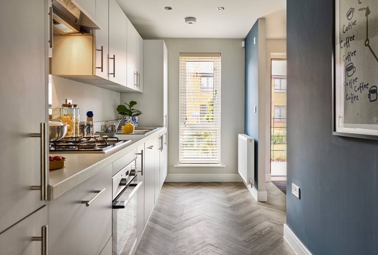 A modern kitchen with white cabinets, a gas hob, an oven, and a window.