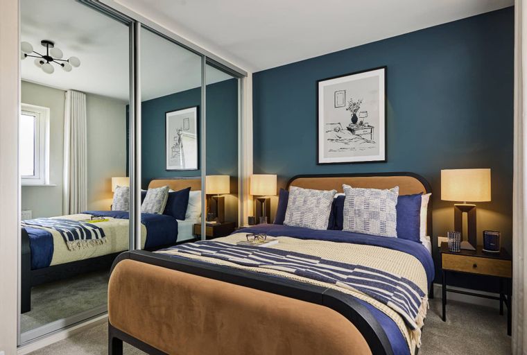 A bedroom with a bed, bedside tables, lamps, and mirrored wardrobes.