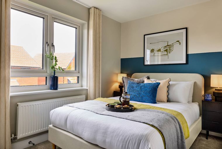 A bedroom with a bed, pillows, a tray with tea, and a window.