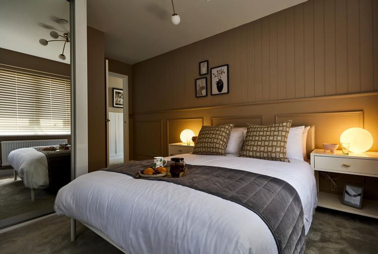 A bedroom with a bed, pillows, bedside tables, and a mirrored wardrobe.