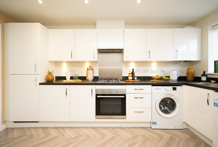 A modern kitchen with white cabinets, black countertops, a gas hob, oven, and washing machine.