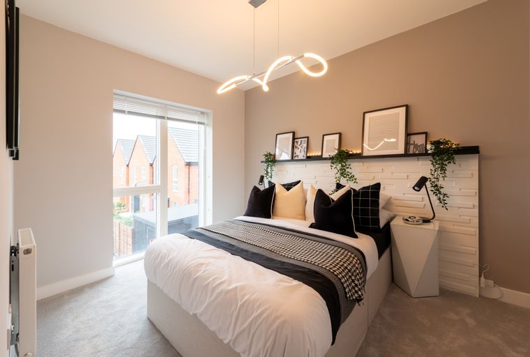 A bedroom with a bed, pillows, a blanket, a bedside table, and a window.