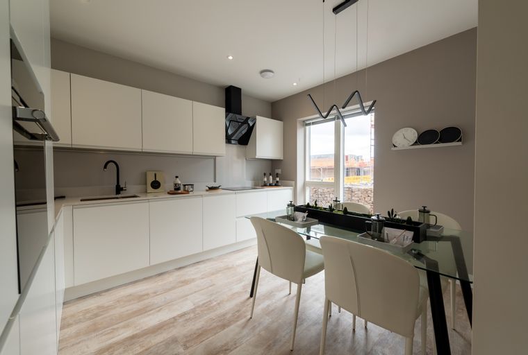 A modern kitchen and dining area with white cabinets, a black range hood, and a glass-top dining table.