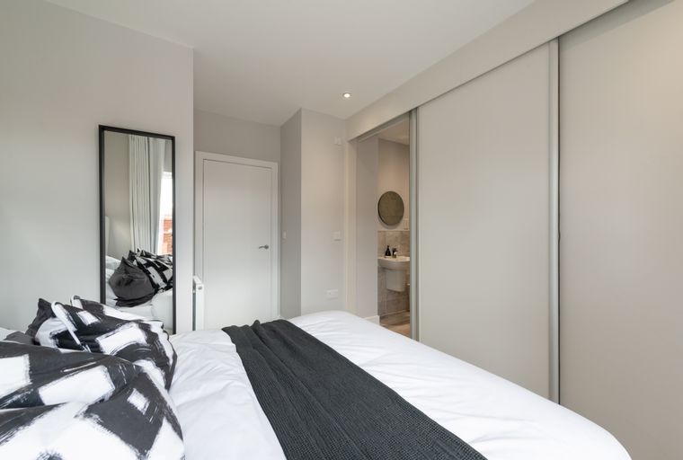 A bedroom with a bed, pillows, a mirror, and a sliding door wardrobe.