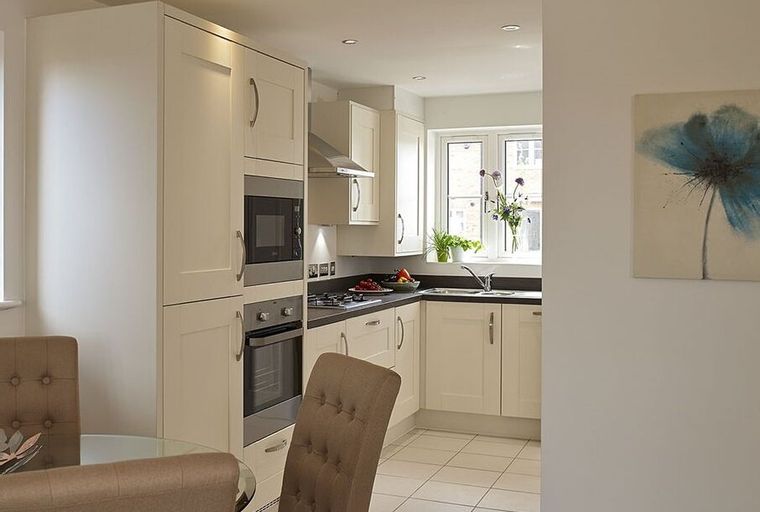 A kitchen with cream cabinets, a microwave, an oven, and a sink under a window.