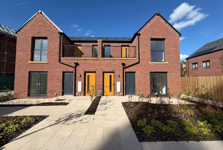 A row of modern red brick townhouses with grey and yellow doors under a blue sky.
