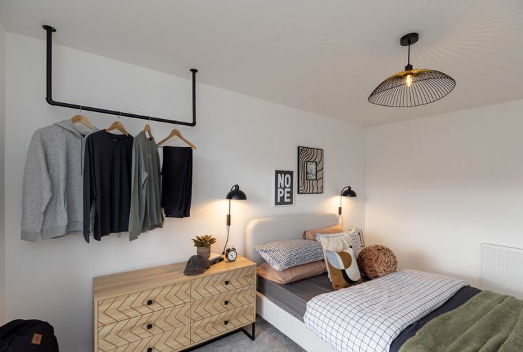 A bedroom with a bed, dresser, and clothing rack.