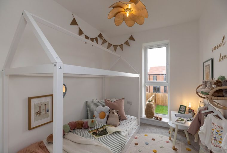 A child's bedroom with a house-shaped bed, stuffed animals, and a window overlooking a garden.