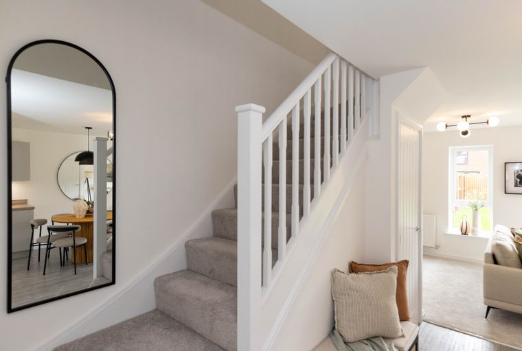 A hallway with a staircase, a mirror, and a bench with pillows.