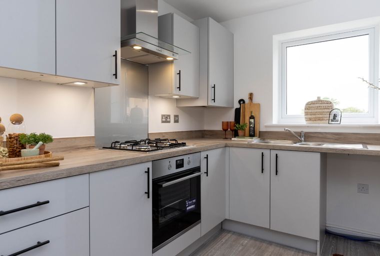 A modern kitchen with light grey cabinets, a gas hob, and a sink under a window.