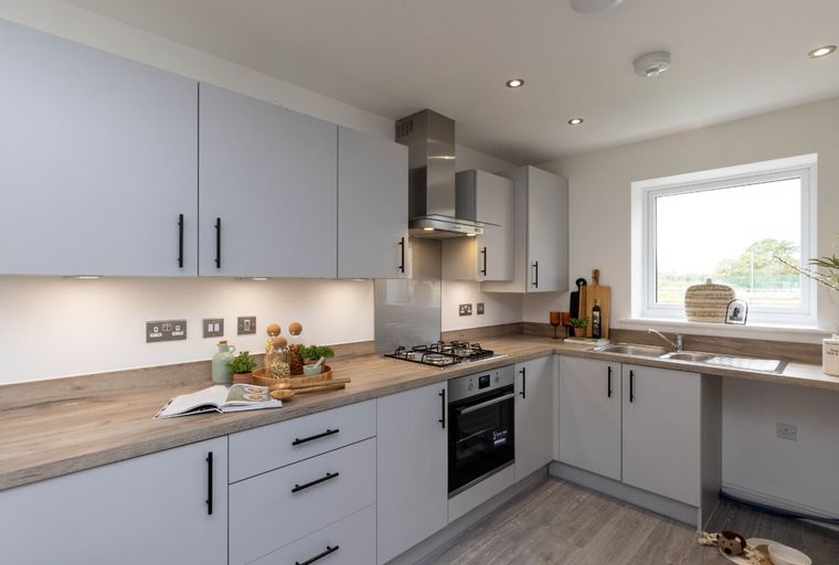 A modern kitchen with light gray cabinets, a wooden countertop, a gas stove, and a sink under a window.