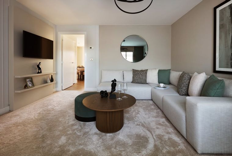 A living room with a sectional sofa, coffee table, ottoman, and a wall-mounted TV.