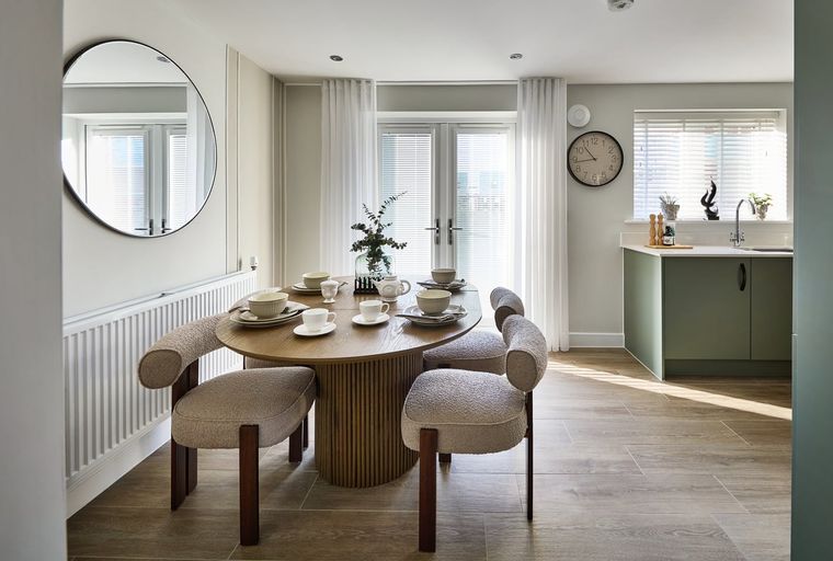 A dining area with a round table, chairs, and a kitchen in the background.
