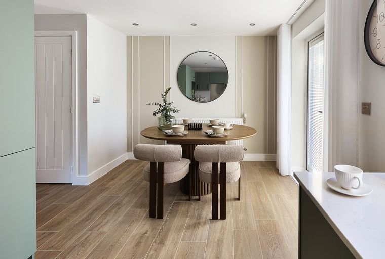 A dining area with a round table, two chairs, and a mirror.