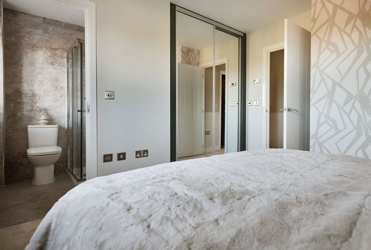 A bedroom with a bed, a mirrored wardrobe, and an en-suite bathroom with a toilet and shower.