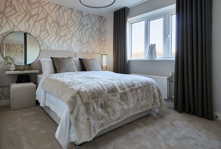 A bedroom with a bed, pillows, a blanket, a mirror, and a window.