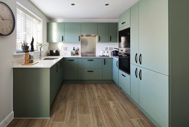 A modern kitchen with sage green cabinets, a sink, and a window.