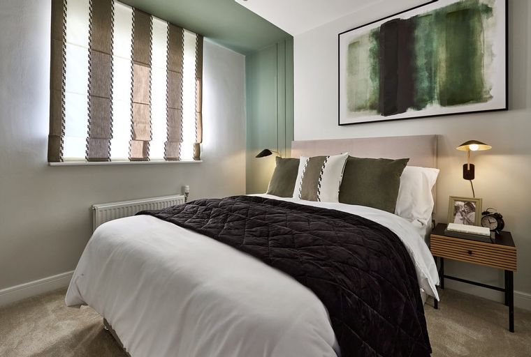 A bedroom with a bed, pillows, a quilted comforter, a bedside table, and a painting on the wall.
