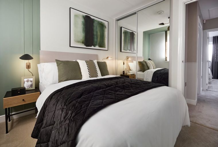 A bedroom with a bed, pillows, a nightstand, and a mirror wardrobe.