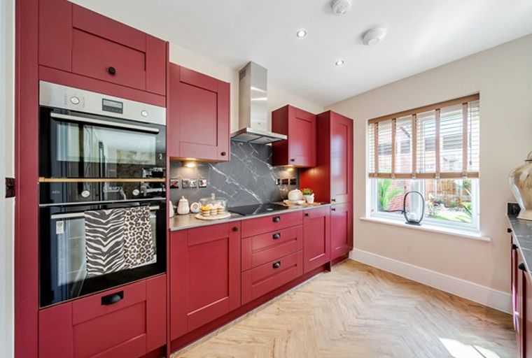 A modern kitchen with deep red cabinets, stainless steel appliances, and a herringbone floor.