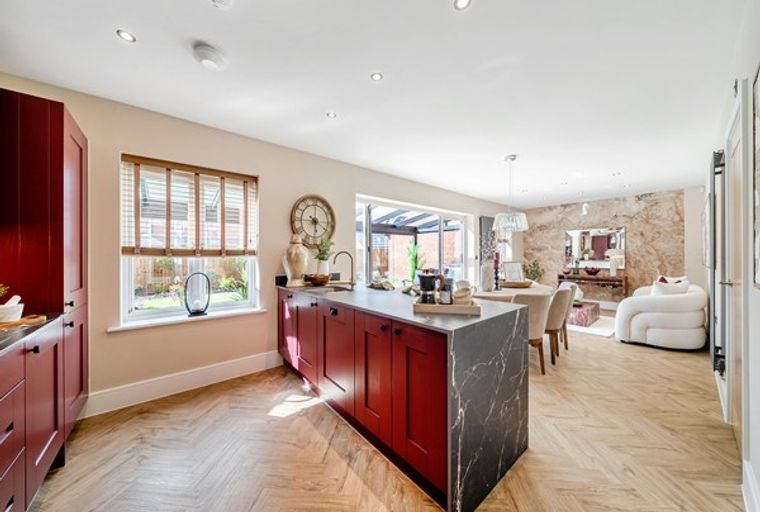 A modern kitchen and dining area with red cabinets, a marble island, and dining furniture.