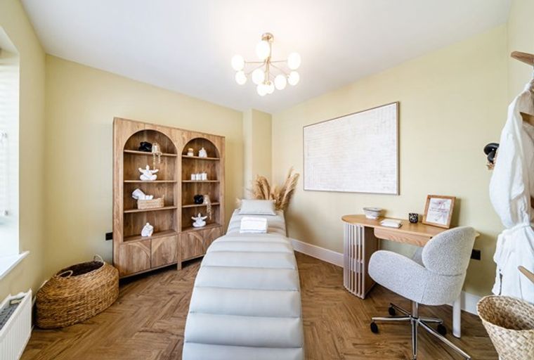 A spa room with a massage bed, wooden shelves, and a desk with a chair.