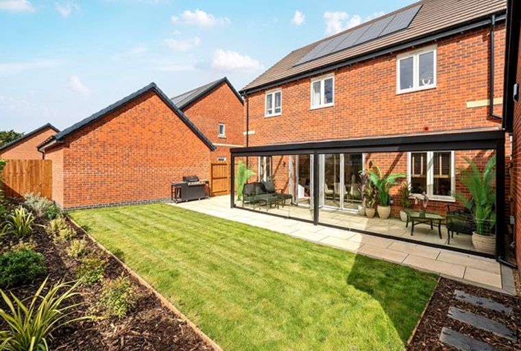 A backyard with a glass conservatory, lawn, and barbecue.