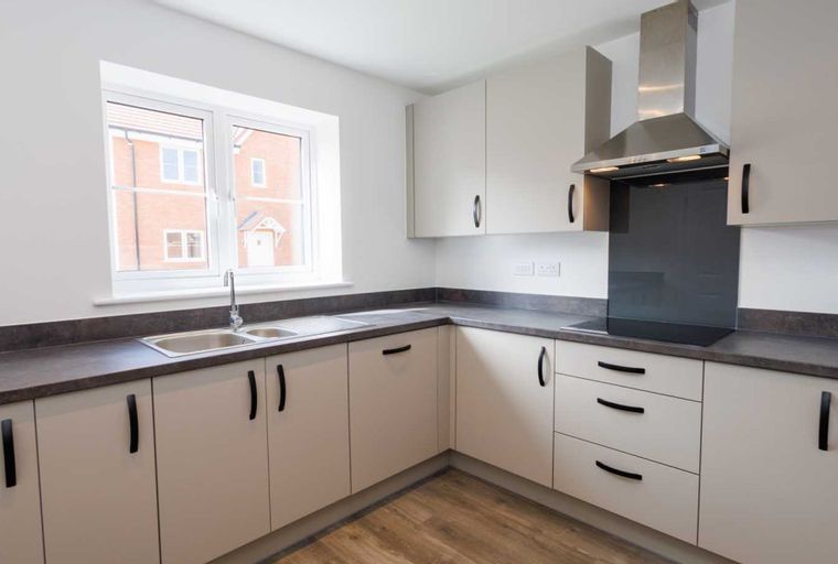 A modern kitchen with cream cabinets, a double sink, and a window.