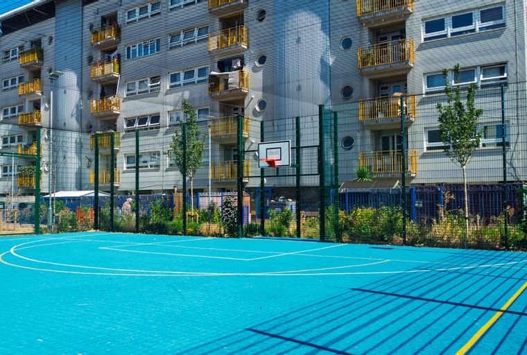 A basketball court in front of an apartment building with balconies.
