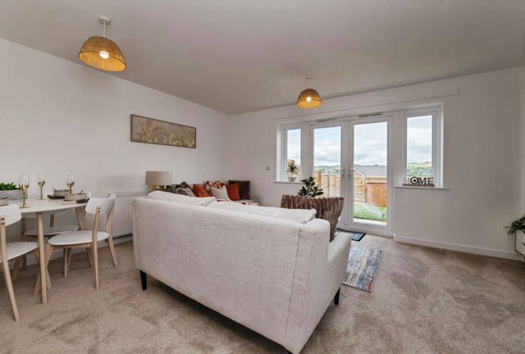A living and dining area with a sofa, dining table, chairs, and French doors leading to a garden.