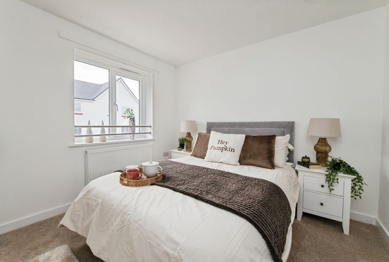A bedroom with a bed, pillows, a throw blanket, and a window.