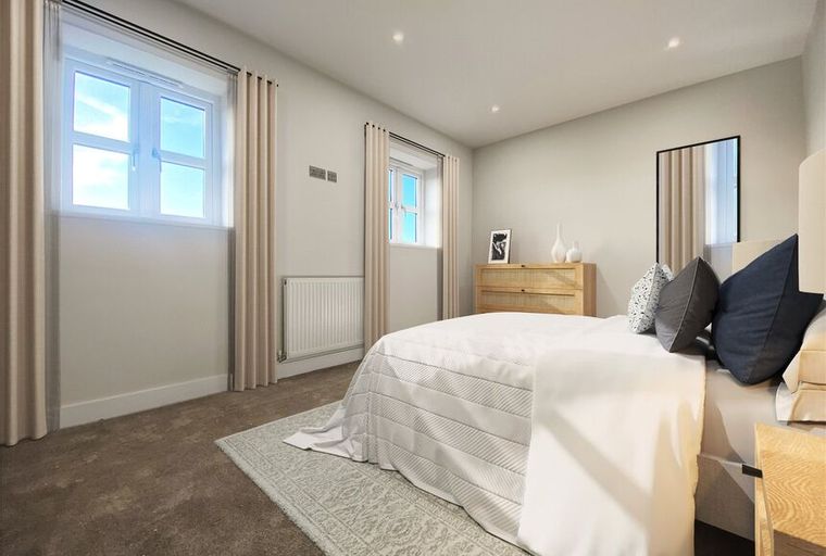 A bedroom with a bed, windows, curtains, and a dresser.