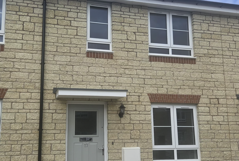 A light beige stone brick house with a grey front door and white-framed windows.