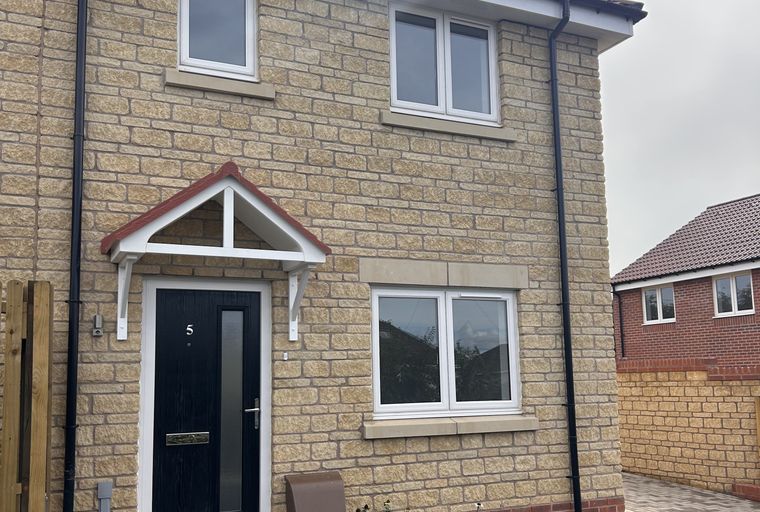 A modern house with light brick exterior, black front door, and white-framed windows.