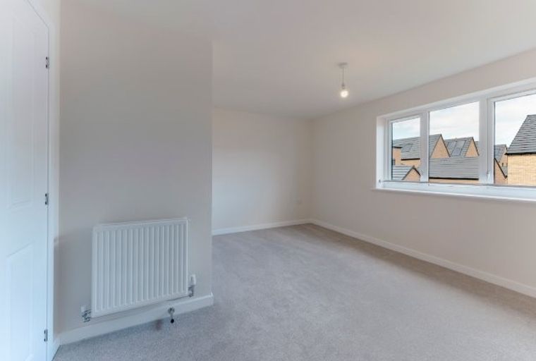 A bedroom with a radiator and a window overlooking houses.