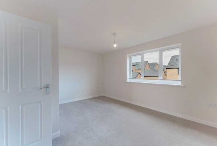 A bedroom with a white door, a window overlooking houses, and grey carpeting.