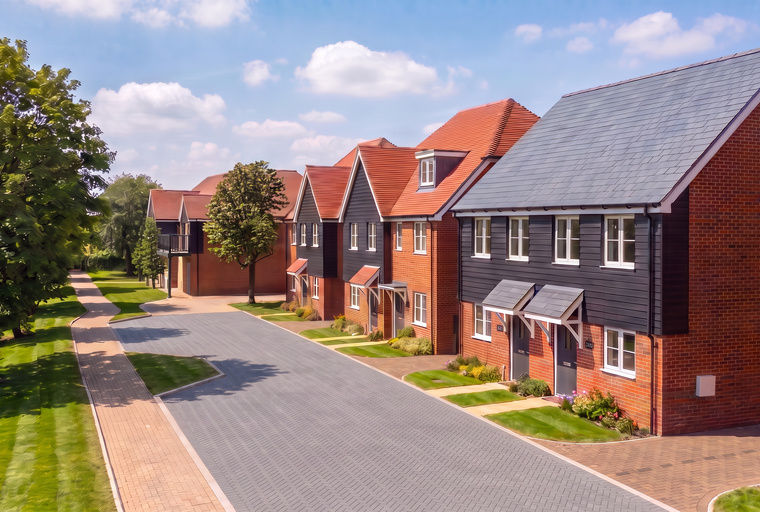 A row of modern townhouses with brick and dark wood exteriors, pitched roofs, and manicured lawns.