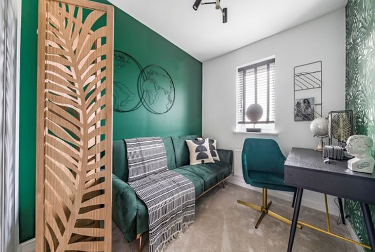 A home office with a green sofa, a desk, and a chair.