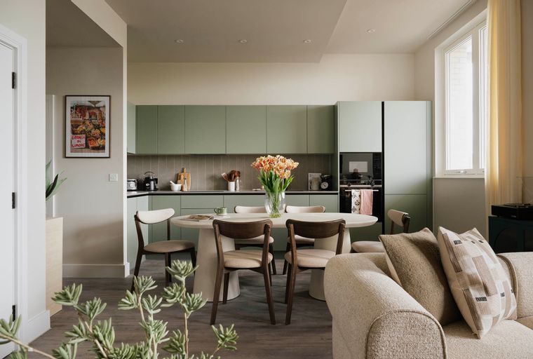 A dining area and kitchen with an oval table, chairs, and sage green cabinets.