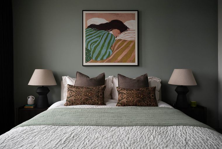 A bedroom with a bed, pillows, lamps, and artwork on the wall.