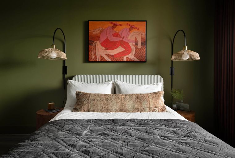 A bedroom with a bed, artwork, and pendant lights.