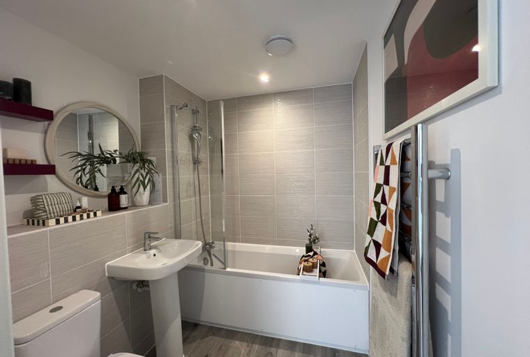 A bathroom with a bathtub, shower screen, sink, toilet, and decorative items.