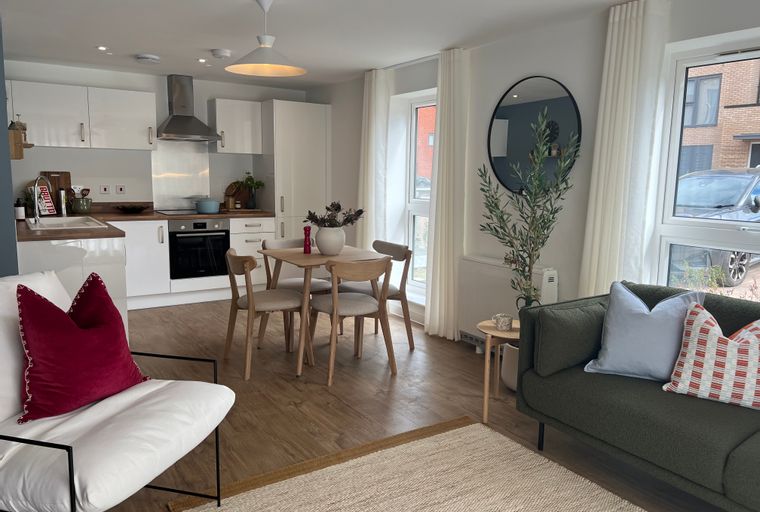 A living room and kitchen area with a dining table, chairs, a sofa, and kitchen cabinets.