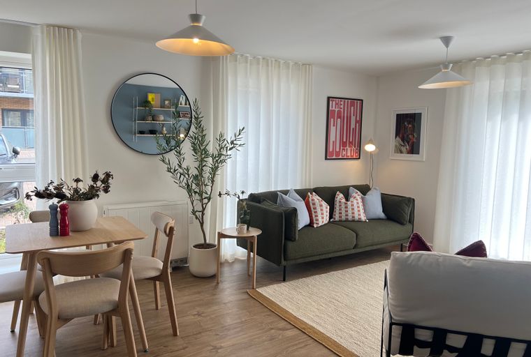 A living and dining area with a green sofa, dining table, chairs, and sheer curtains.