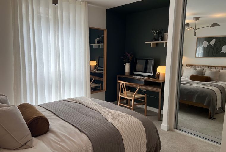 A bedroom with a bed, a desk, and a mirrored wardrobe.