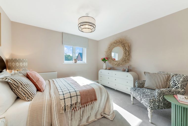 A bedroom with a bed, dresser, mirror, and armchair.